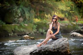 Girl in dark glasses sits on stone on Riverside