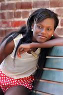 photo of a dark-skinned girl on a bench against a brick wall