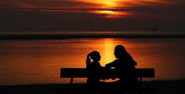 Child Daughter and Mother sitting on bench in front of water at dusk