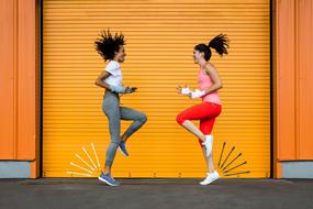 Smiling women, doing exercises, near the orange wall