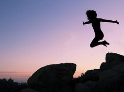 Girl jumping above Rock, silhouette at evening sky