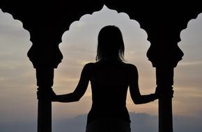 Silhouette of a woman, among the columns, at beautiful and colorful sunset, in India