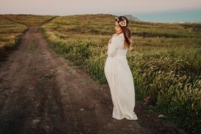 Posing woman in white dress, on the road, among the beautiful and colorful fields