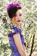 Asian girl with a purple floral wreath on her head against a background of a blossoming tree