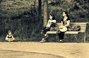 two Women sitting on bench an child girl on walk path in park