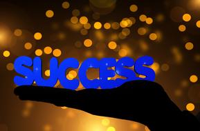 success, blue letters on hand at bokeh background