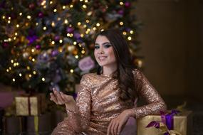 beautiful Girl in golden dress sits in front of Christmas Tree