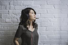 beautiful girl in black headphones near a white brick wall