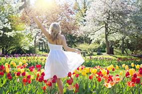 Pretty Young Woman in white dress stands on flower bed among Tulips