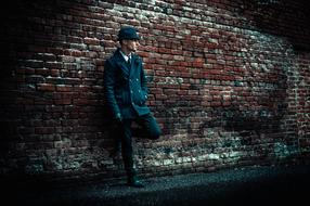 Man in black stylish clothing leaning on brick wall