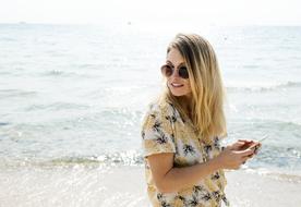 Blonde girl with sunglasses, using phone on the sandy beach
