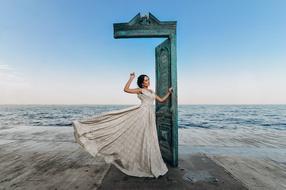 young Woman in long dress stands in doorway in front of sea, collage