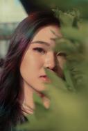 portrait of an asian woman behind green leaves on a blurred background