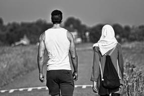 Man and Woman in white headscarf walking away on road