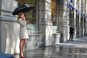 posh young Woman beneath umbrella waiting at wall in city