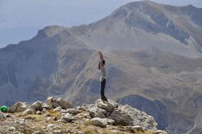 Girl standing on rock with hands up at scenic mountain