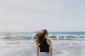 Back view of the girl with sunglasses and jeans, on the beautiful coast with waves
