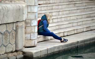 young girl sits on stone steps at water