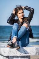 photo of a girl in a leather jacket and ripped jeans against the sea