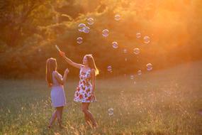 two young Girls plays with soap bubbles at Sunset