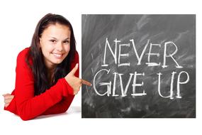 Smiling woman in red clothing, near the white chalk "Never Give Up" sign on the blackboard, at white background