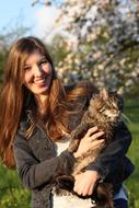 smiling girl holding a cat in her arms in the garden