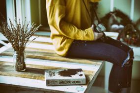 girl sits on wooden table beside of Book