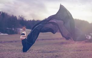 photo of a pregnant girl in a mask and an air dress on the field