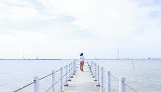 Girl stands on Pier looking at calm sea