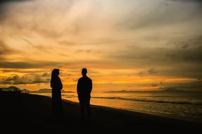 male and female silhouettes on beach at dusk