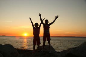 children with hands up at sunset