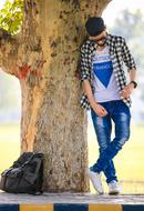 boy in fashion clothes stands beneath big tree