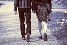 Black and white photo with the back view of the walking couple, holding hands together, on the road