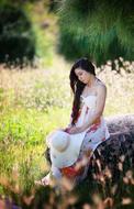 young asian Girl sits on stone with white wide hat in hands