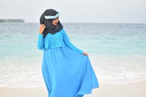 Muslim woman in blue long dress and black Hijab posing at sea