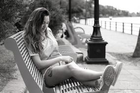 Black and white photo of the girl, sitting on the bench, on the beautiful coast with the fence