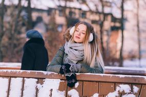 young girl in scarf on neck standing at fence on snowy winter