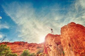 Woman, standing on the beautiful and colorful rock cliff, among the desert with green plants, in sunlight