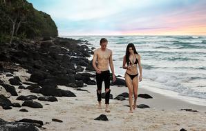 young Man and Woman in bikini walking on beach at sunset