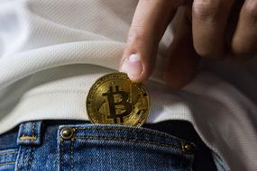 bitcoin in male hand at pocket of jeans pants