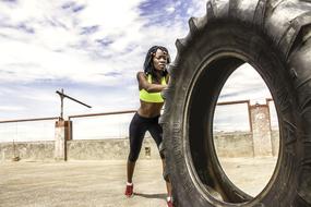 sportive dark skin woman pushing giant tire outdoor