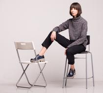 Young woman in stylish shoes sits on black chair with foot on white chair