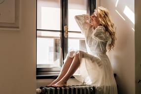 Blonde woman in white dress, posing near the window with light