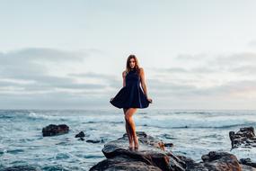 young girl in stylish short dress posing on rock at sea