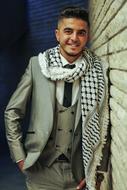 smiling arabian man in luxury tie suit leaning on wall