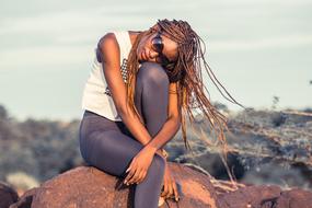 African woman in sunglasses, posing on the rock, in summer