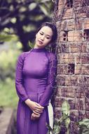 Girl in violet dress, posing near the brick wall, among the plants in Vietnam