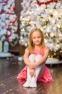 Smiling, blonde girl, near the colorful and beautiful Christmas tree, with the lights and snow, on the Christmas