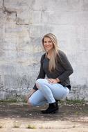 Beautiful, smiling blonde girl in jeans, posing near the wall