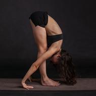 Woman in black clothing, doing stretching, at black background, in light